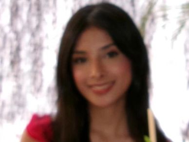 Young woman smiling with long dark hair and blurred background.