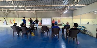A group attending a presentation in a spacious room with blue flooring.