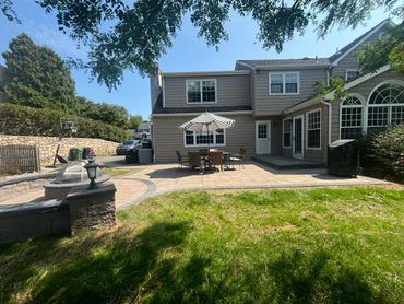 Spacious backyard patio with outdoor dining set and umbrella beside a two-story house.