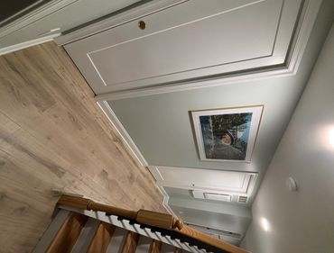 A hallway with wooden stairs, light gray walls, and a framed picture.