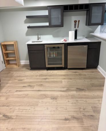 Modern kitchenette with dark cabinets, a mini fridge, and a wooden floor.