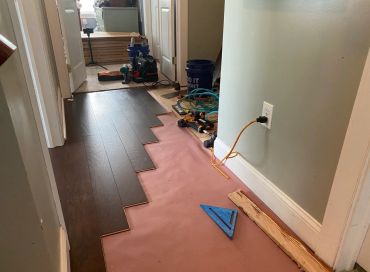 Partially installed dark wood flooring with tools and pink underlayment visible.