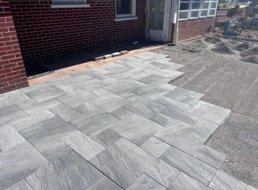 Newly installed gray stone patio outside a brick house under construction.