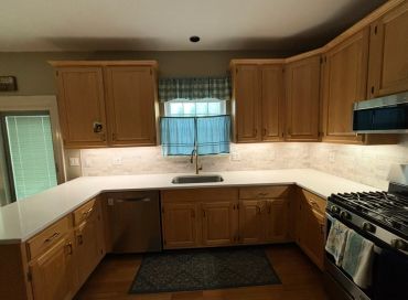 Cozy kitchen with wooden cabinets, white countertops, and a window with blue curtains.