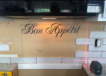 Kitchen wall with 'Bon Appétit' decal amid tile installation.