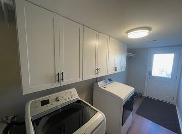 A modern laundry room with washer and dryer under white cabinets.