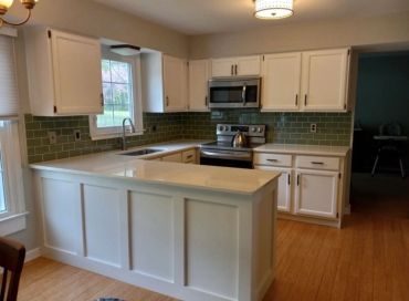 Modern kitchen with white cabinets and green tile backsplash.