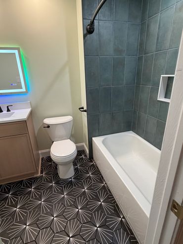 Modern bathroom with patterned floor, white bathtub, and illuminated mirror.