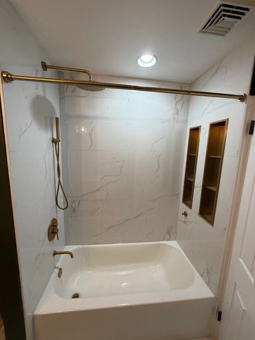 Modern bathroom with white marble walls and gold fixtures.