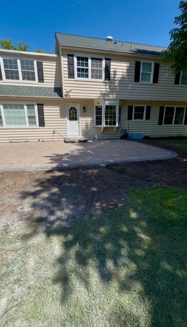 Newly paved patio in backyard of a beige two-story house.