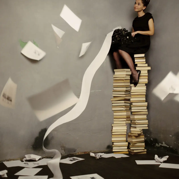 Woman sitting on a tall stack of books using a typewriter.