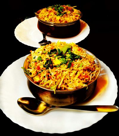 Two bowls of flavorful biryani garnished with fresh herbs on white plates.
