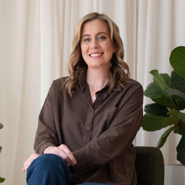 Smiling woman sitting on a green chair with plants in the background.