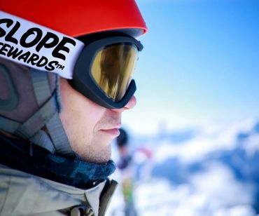 Close-up of a skier wearing a red helmet and goggles with a snowy mountain backdrop.