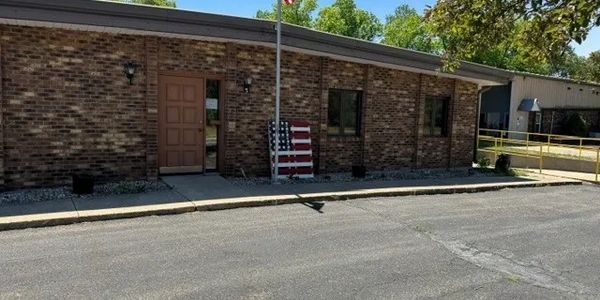 Brick building with a wooden door and American flag decoration outside.