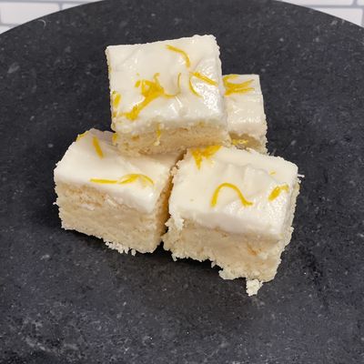 Four pieces of frosted lemon cake on a dark plate.