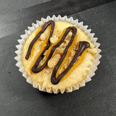 A cupcake with caramel, chocolate drizzle, and nuts on top.