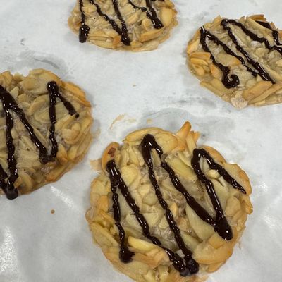 Almond cookies drizzled with chocolate on parchment paper.