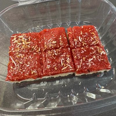 Six pieces of red dessert with shredded toppings in a clear container.