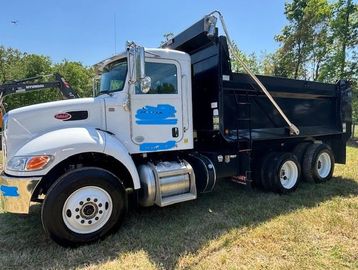 White dump truck with black bed parked on grass under blue sky.
