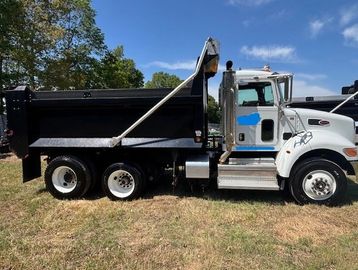 White and black dump truck parked on grass under blue sky.
