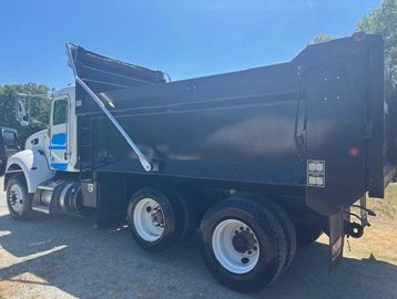 Side view of a black dump truck under clear blue sky.
