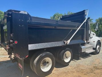 Black dump truck parked on a dirt surface under clear blue sky.