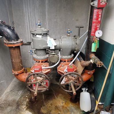 Industrial pipes and valves in a maintenance room with cleaning tools nearby.
