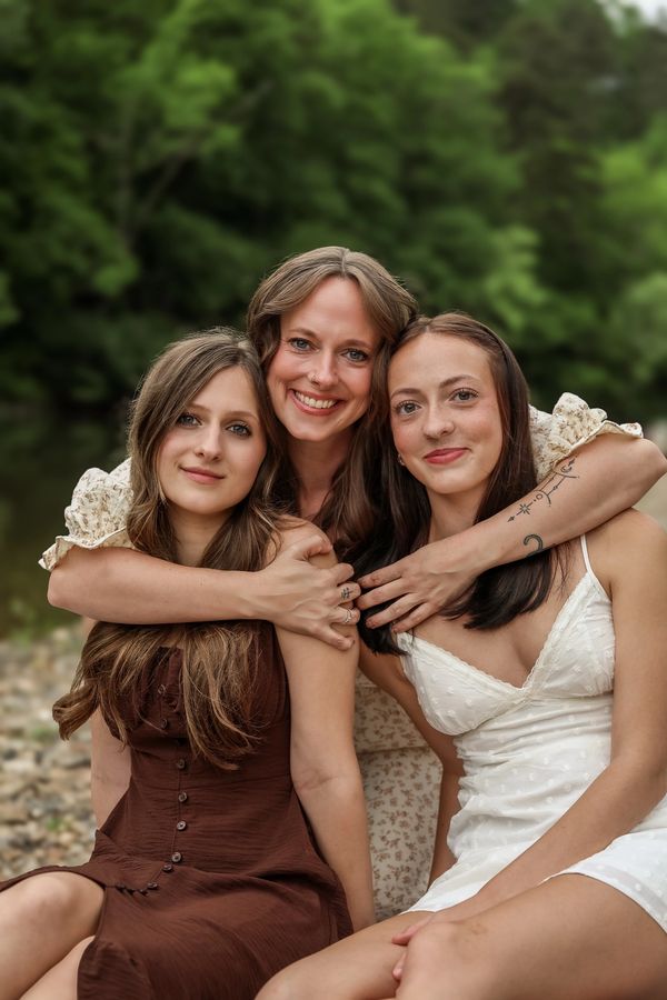 Three women sitting close together outdoors, smiling warmly.