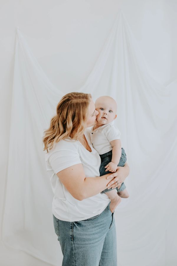 Mother lovingly kisses her baby boy in a bright, white setting.