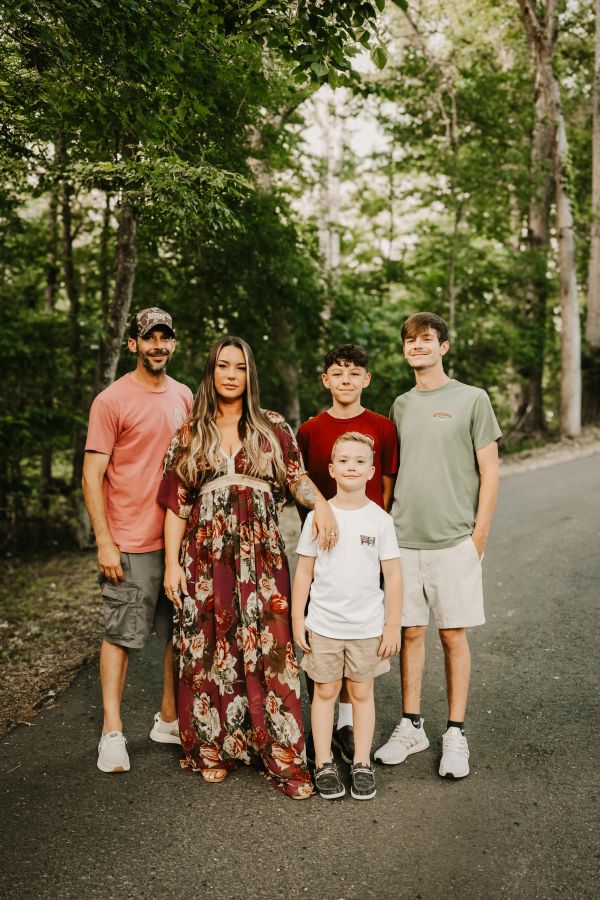 A family of five posing outdoors on a tree-lined path.