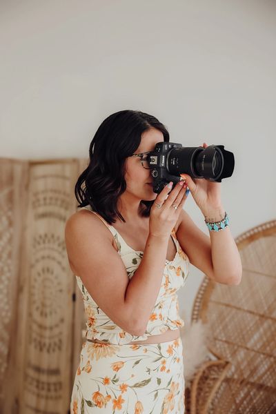 Woman with glasses taking a photo with a Canon camera indoors.