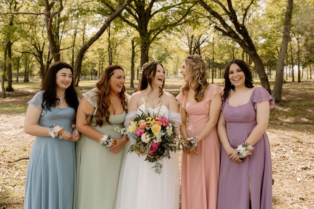 Bride with her bridesmaids laughing in the woods at the premier waterfront wedding venue in Texas.
