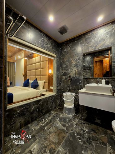 Modern bathroom with dark marble tiles and a view into a cozy bedroom.