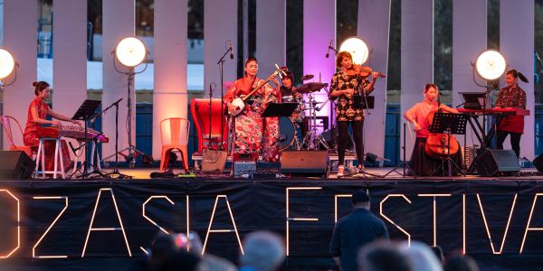 A diverse musical band performing on stage at OZASIA Festival.