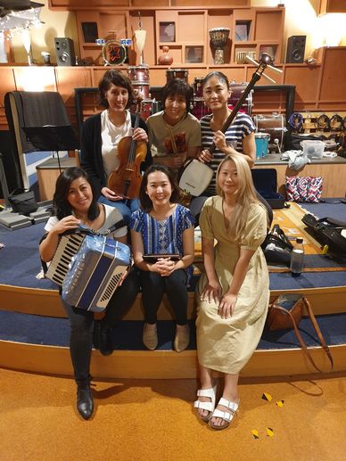 Group of six women with musical instruments posing indoors.