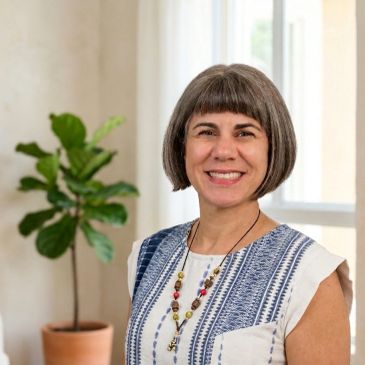 Smiling woman with a bob haircut and patterned top indoors.