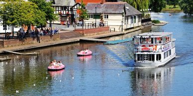 Boats and pedal boats on a calm river near a lively riverside area.
