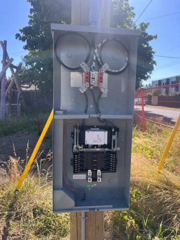 Open electrical panel outdoors with wiring and circuit breaker.