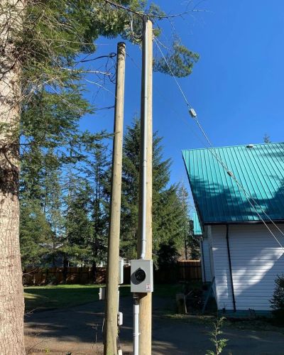 Utility poles next to a house with a green roof under a clear blue sky.