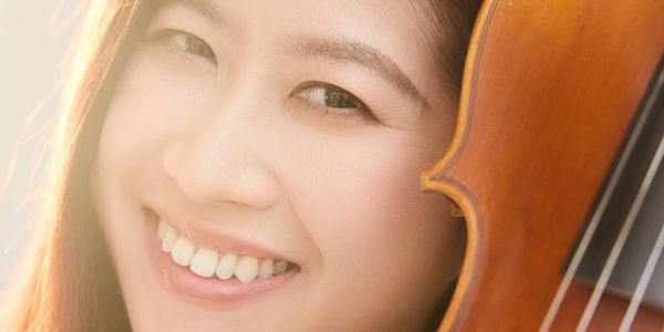 Young woman smiling with a violin next to her face.