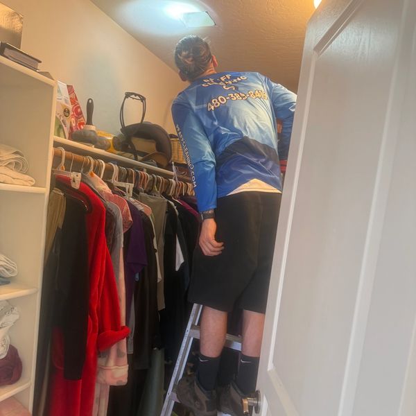 Person on a ladder reaching for something in a closet.