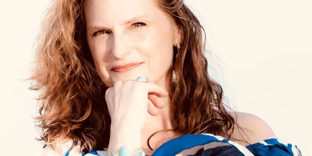 Portrait of a woman with curly hair resting her chin on her hand.