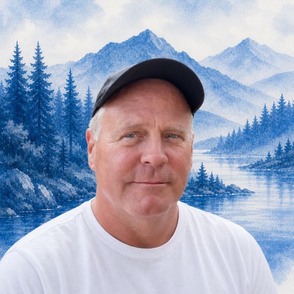 Man wearing a black cap with a blue mountain landscape background.