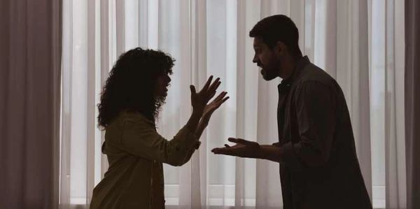 Silhouetted couple arguing at home in pajamas with light streaming through the room behind them.