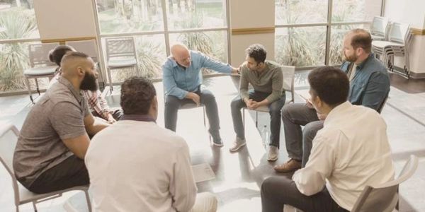 Overhead view of men sitting in a circle during a group coaching or therapy session.