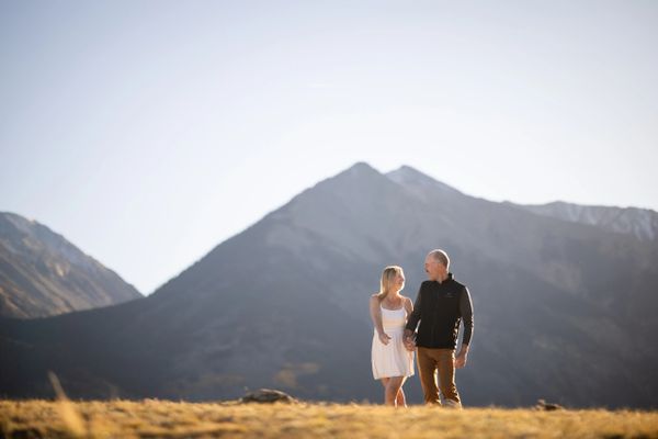 Couple walking hand-in-hand in front of large mountains on a sunny day.