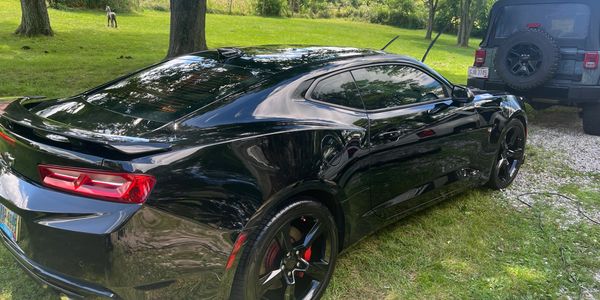 Sleek black sports car parked on grass near trees and a black SUV.