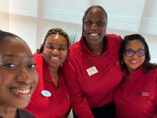 Four smiling women in matching red tops posing indoors.