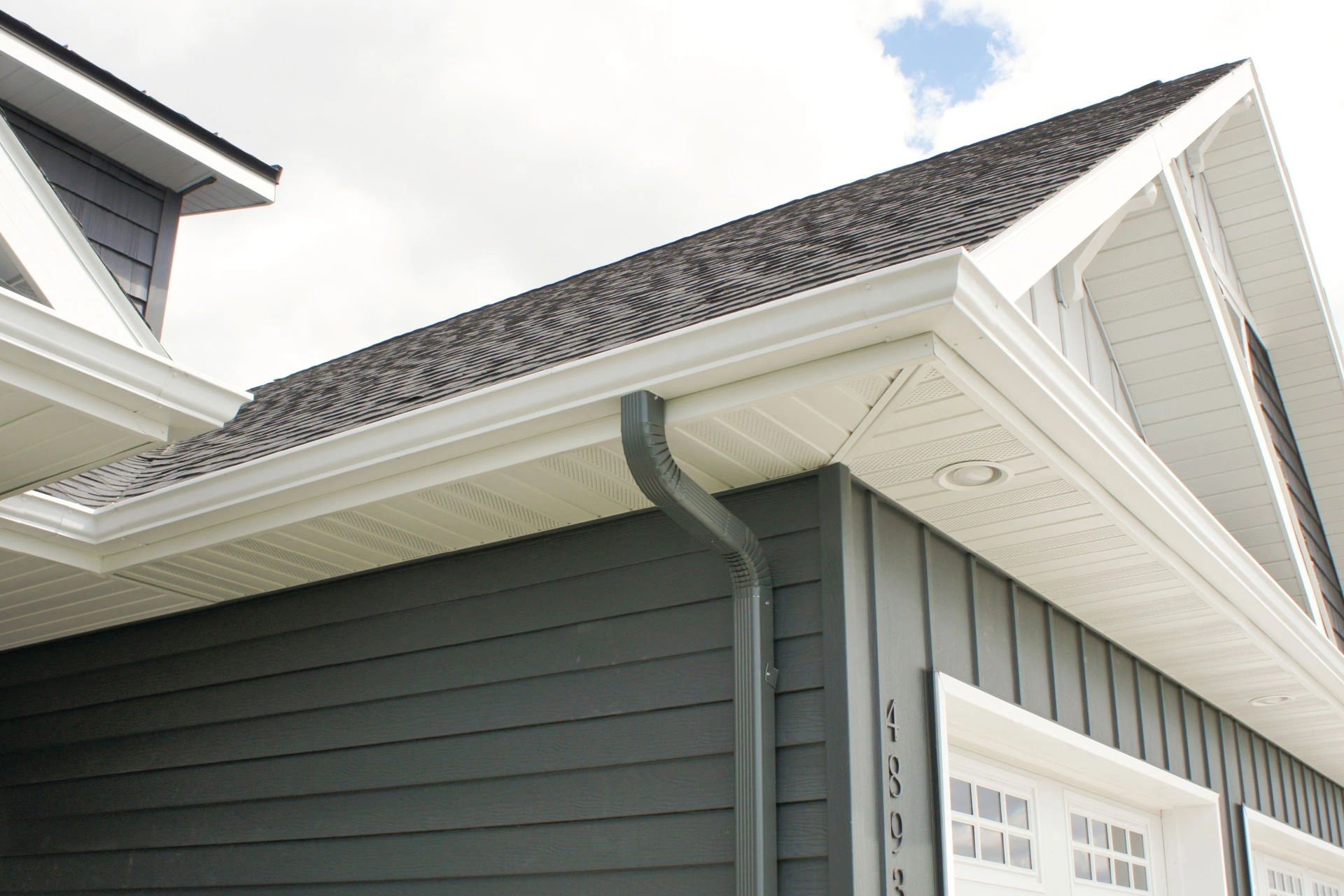 Modern house exterior with dark siding and white trim under a partly cloudy sky.
